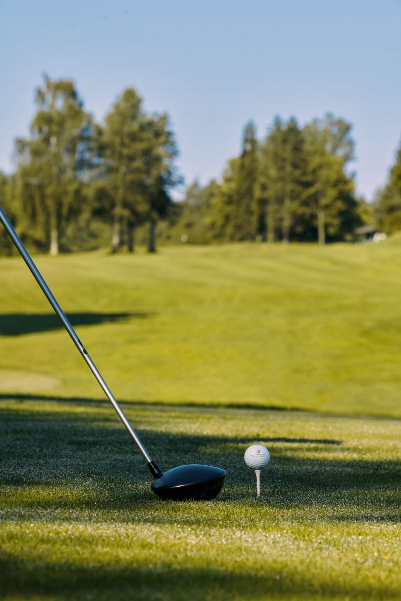 Golf-Abschlag: Golfschläger und Golfball auf grüner Wiese zum Abschlag bereit