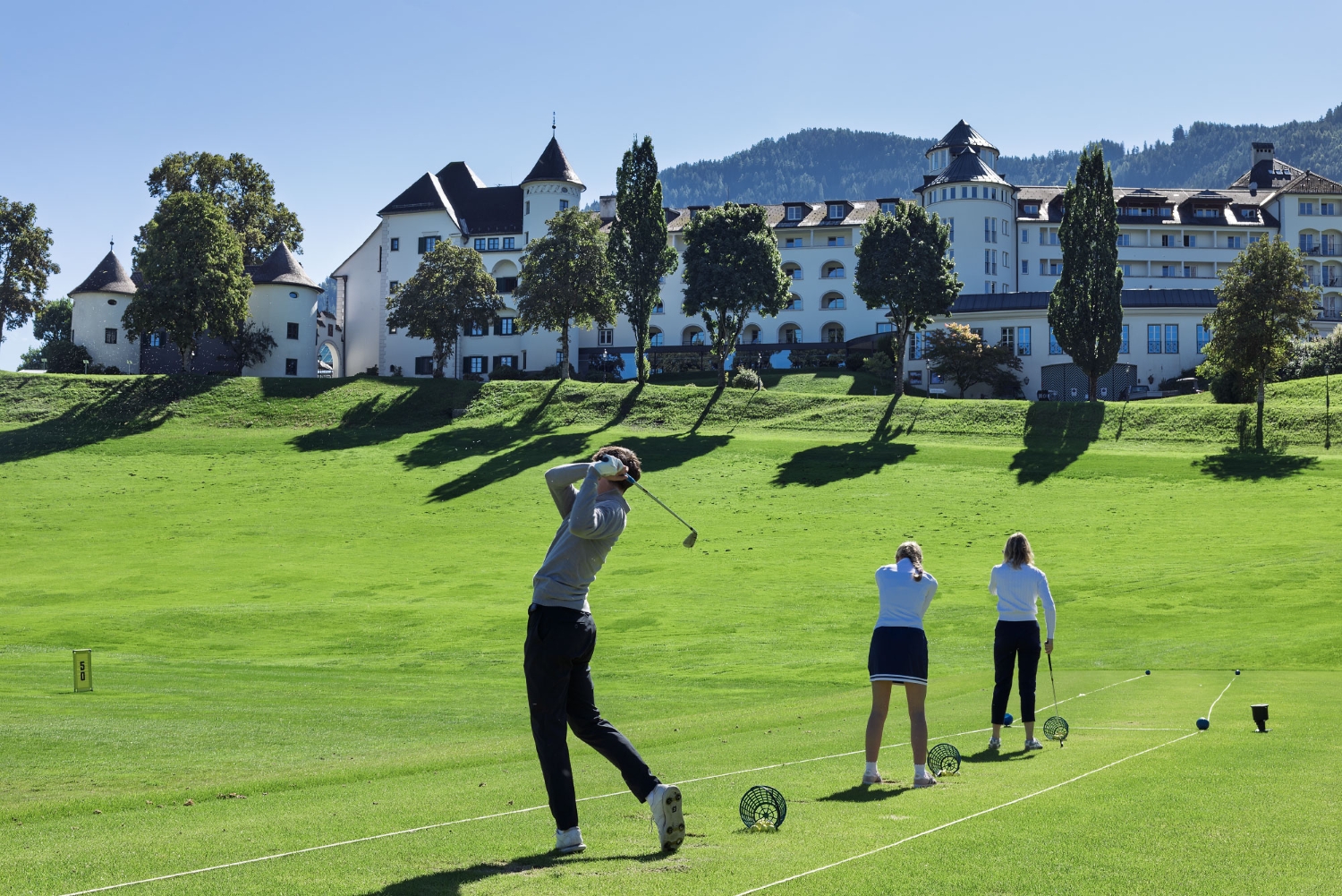 Bild: Golfspieler*innen auf der TrackMan Range mit Blick auf das IMLAUER Hotel Schloss Pichlarn